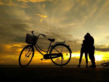 Silhouette man standing by bicycle against sky during sunset