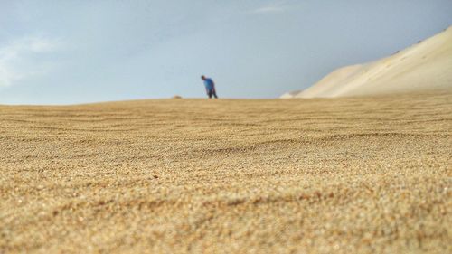 Man walking on sand dune at beach against sky
