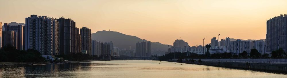 River amidst buildings against sky during sunset