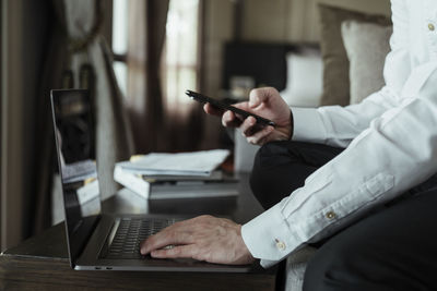 Midsection of man using mobile phone while sitting on table