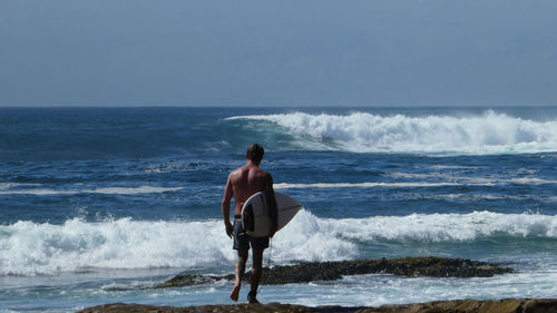 Rear view of shirtless man standing at beach against sky