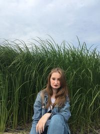 Portrait of beautiful young woman sitting against plants on field