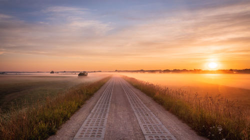 Road amidst field against sky during sunset