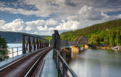 Railway bridge over river against cloudy sky