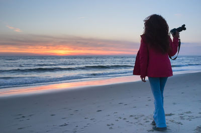 Woman standing on beach against sky during sunset