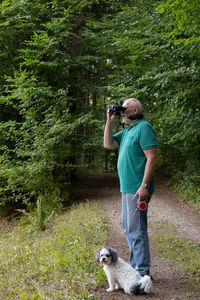 Man is watching nature with binoculars while his dog sits down