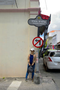 Full length of woman standing by road sign against wall