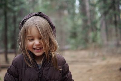 Cute cheerful girl wearing warm clothing standing in forest