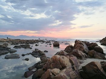 Rocks on shore against sky during sunset