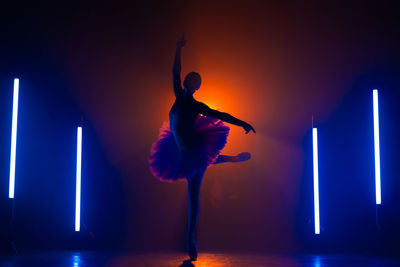 Silhouette of ballerina is practicing elements in studio with neon light. young woman dancing