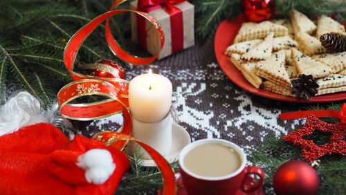 Cup of hot coffee with homemade shortbread cookies and red christmas decor on a knitted background 