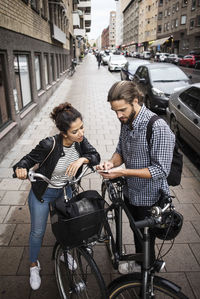 High angle view of friends with bicycles looking at phone while standing on sidewalk in city