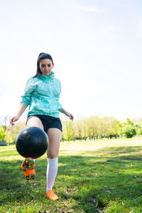 Full length of young woman playing soccer on field against sky