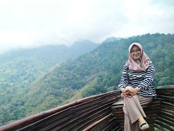 Portrait of smiling young woman wearing hijab sitting against mountains and sky