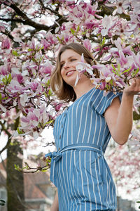 Blonde with pleasure inhales an aroman of magnolia flowers standing under a tree