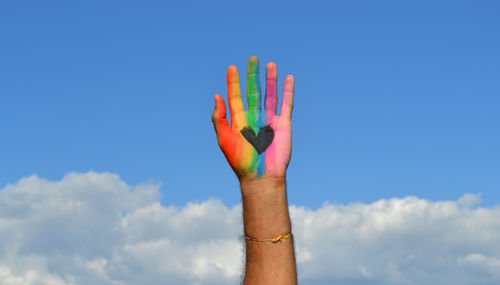 Cropped hand showing heart shape paint against blue sky