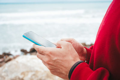 Midsection of person holding mobile phone against sea