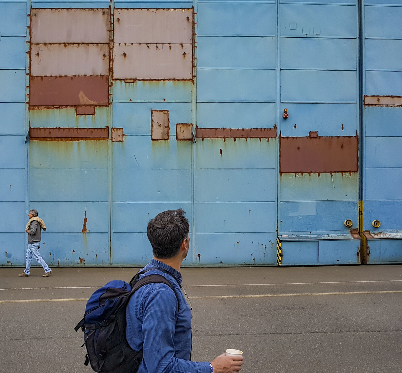 REAR VIEW OF MAN SITTING AGAINST BUILDING