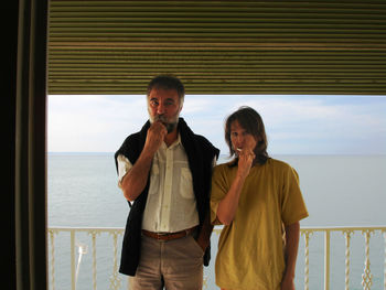 Portrait of man and woman brushing teeth while standing at balcony against sea