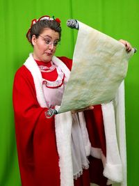 Mid adult woman in costume reading paper while standing against green curtain