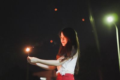Beautiful woman holding sparkler at night