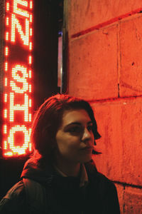 Portrait of young woman looking away against brick wall