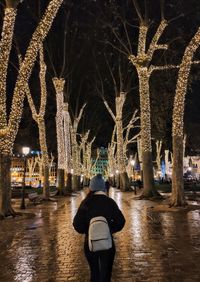 Rear view of man walking on illuminated street at night