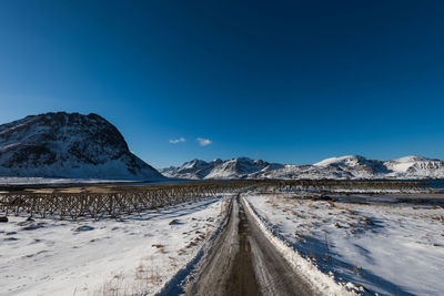 Road leading towards snowcapped mountains against blue sky