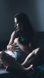 Side view of young woman sitting on bed at home