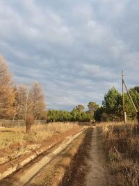 Dirt road amidst field against sky