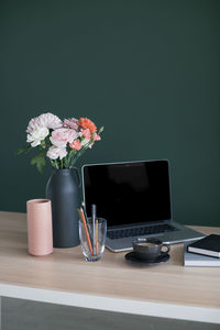 Flower vase by laptop on table at home