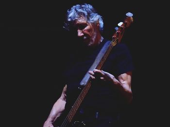 Man playing guitar against black background