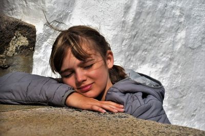 Portrait of woman lying on rock against wall