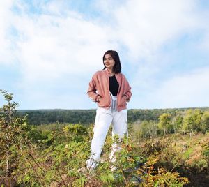 Young woman standing on field against sky