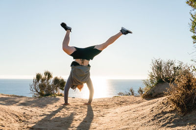 Man doing handstand on beach against clear sky