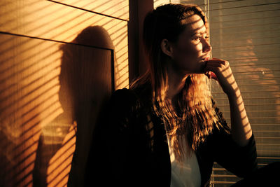 Young woman looking through window at home