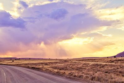Road by landscape against sky during sunset