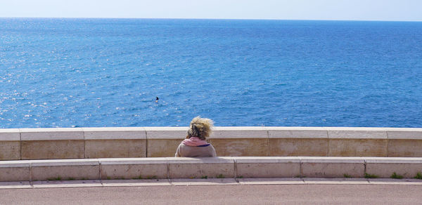 Rear view of woman sitting against blue sky