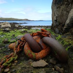 Rusty metal on rock by sea against sky