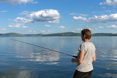 A woman fisherman catches fish for a bait from a blue lake on the background of a mountainous coast.