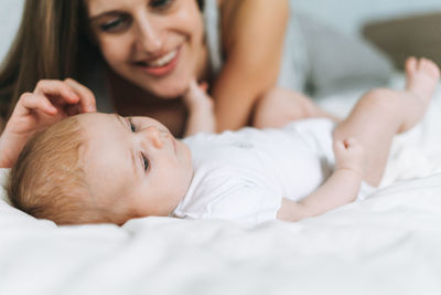 Young mother having fun with cute baby girl on the bed with white linen, natural tones, love emotion