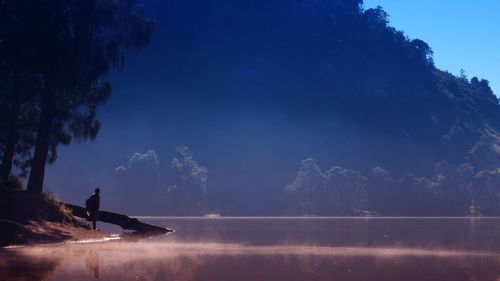 Silhouette of person standing at lakeshore
