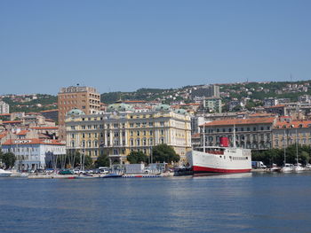 Sailboats in sea by buildings against clear sky