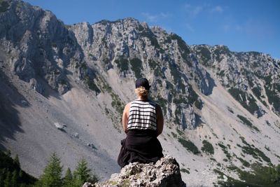 Rear view of woman sitting on rock against mountain