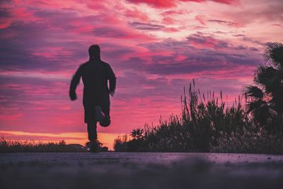 Silhouette man standing by trees against orange sky