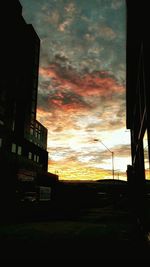 Silhouette buildings against cloudy sky at sunset