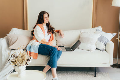 Thoughtful attractive relaxed woman using laptop for media sitting on sofa in living room