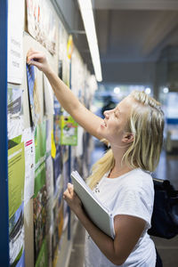 University student tacking paper to bulletin board in college