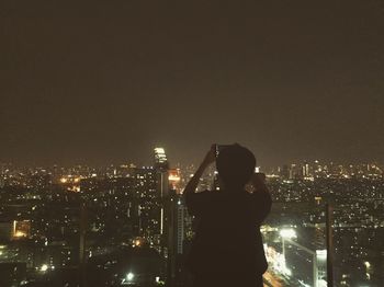 Man looking at illuminated cityscape against sky at night