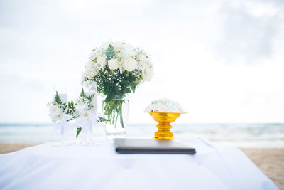 Close-up of white flowers and wineglasses on table at beach